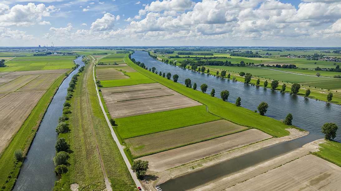 Foto van Capelsche uiterwaard met groen en bruin landschap met twee rivieren die langs het land lopen.